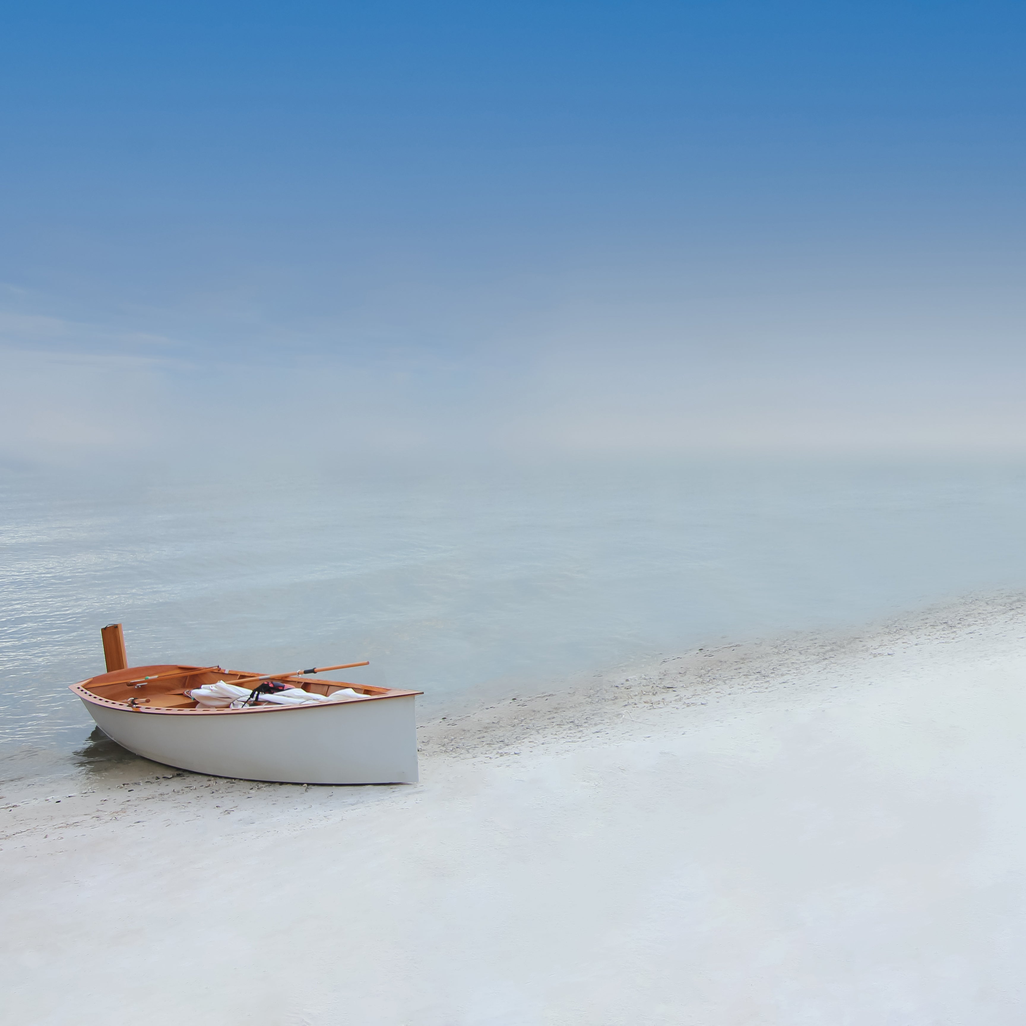 "Castaway" photograph of a lone wooden boat partially on blue ocean, partially on the sand of the beach